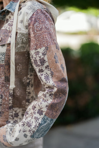 Close-up view focusing on the rich sleeve texture and fabric print layout of a boho patchwork jacket. Highlights the seamless blend of floral and paisley patches in warm brown, cream, and dusty blue tones alongside the flat cream hoodie drawstring.