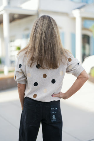 Back view of the Polka Dot Short-Sleeve Knit Sweater showing the continuous multi-colored polka dot pattern across the shoulders and back. Highlights the comfortable, relaxed fit and fine ribbed hem worn over black denim jeans.