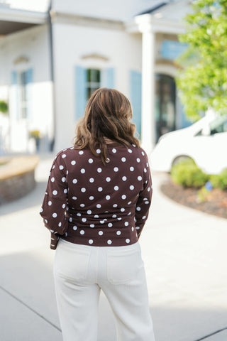 Back view showcasing the fit of the chocolate brown polka dot long-sleeve top and cream corduroy pants. Highlights the seamless polka dot pattern across the shoulders and back, along with the back pocket placement and straight-leg cut of the cream trousers.