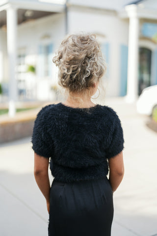 Back view of a woman wearing the black cropped eyelash knit short-sleeve sweater, showcasing the plush texture, clean crew-neck cut, and cropped waistband fit.