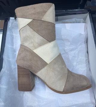 Pierre Dumas mid-calf suede bootie featuring an abstract colorblock patchwork design in neutral tones of beige, taupe, tan, and cream. The structured boot displays a pointed or almond-style toe, a high stacked wooden block heel, exposed accent stitching along the geometric color panels, and a discrete metallic back zipper closure.