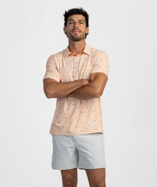 Man standing against a white studio studio background with arms crossed, wearing the Touchdown In Tennessee Polo. The short-sleeve performance polo features a white base with an all-over micro-print of orange and navy state of Tennessee silhouettes. Styled for gameday with light grey active shorts.