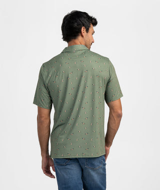 Back view of the Mallard In Motion Polo highlighting the continuous flying mallard duck pattern across the back and short sleeves. Shows the classic fit silhouette, clean self-fabric collar, and subtle straight hemline worn over medium-wash denim jeans against a solid light background.